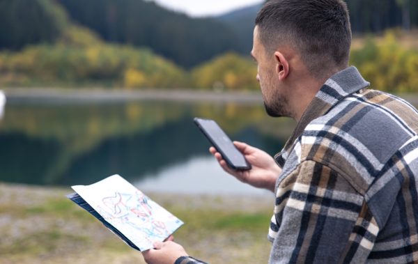 A young man with a map in his hands against the backdrop of mountains.
